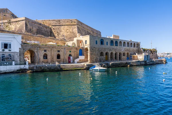 Valletta, Malta - 8 Nisan 2024: Slayema-Valletta feribot sahasının yakınındaki tarihi kireçtaşından yapılmış binaların ve tahkimatların temiz bir gökyüzü altında sakin mavi liman suyunda bulunan küçük teknelerin görüntüsü