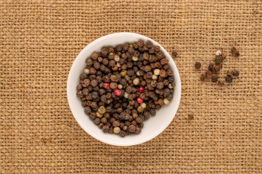 Dry peppercorns, as a spice, on jute cloth, top view.