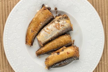 Sprats on a ceramic white plate on kraft paper, top view, macro.