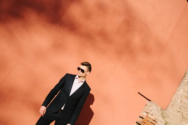 Jovem em um terno preto em um fundo de uma parede de tijolo — Fotografia de Stock