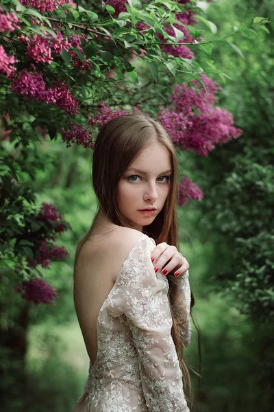 Schönes junges Mädchen in einem blühenden Flieder — Stockfoto