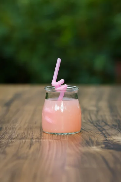 Баночка з рожевим грейпфрутним коктейлем на зеленому фоні боке — стокове фото