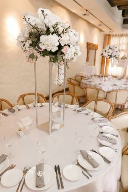Düğün ziyafeti masalarında beyaz renkli çatal bıçaklı şenlikli çiçek dekoru. Farklı doğal renklerde güller, şakayıklar, anturyum. Lüks düğün, parti, doğum günü.