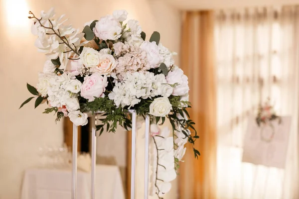 Festive Floral decor on wedding banquet tables in white colors with cutlery. With different natural colors roses, peonies, anthurium. Luxury wedding, party, birthday.