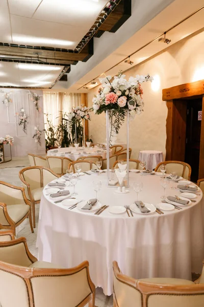 Festive Floral decor on wedding banquet tables in white colors with cutlery. With different natural colors roses, peonies, anthurium. Luxury wedding, party, birthday.