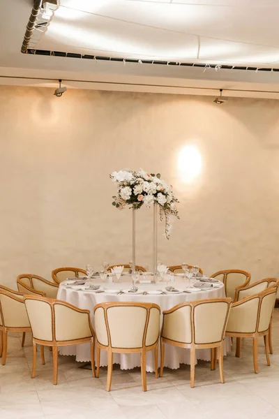 Festive Floral decor on wedding banquet tables in white colors with cutlery. With different natural colors roses, peonies, anthurium. Luxury wedding, party, birthday.