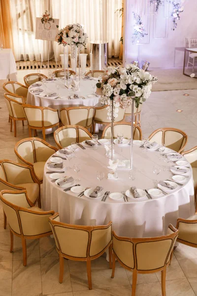 Festive Floral decor on wedding banquet tables in white colors with cutlery. With different natural colors roses, peonies, anthurium. Luxury wedding, party, birthday.