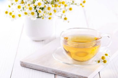 Sağlıklı papatya çayı, beyaz ahşap arka plan fotokopi alanı üzerinde cam bir fincanda.