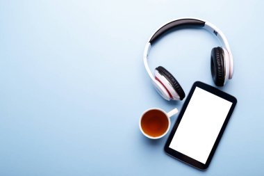 Tablet, kulaklıklar ve mavi arka planda bir fincan çay, düz kopya alanı, maket