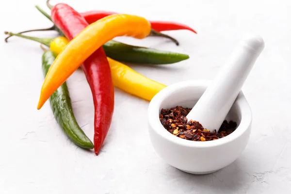 Colorful chili peppers and flakes on grey stone background copy space top view