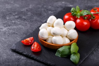 Mozzarella cheese, basil and tomato cherry on black stone tabe copy space. Ingredients for Caprese salad