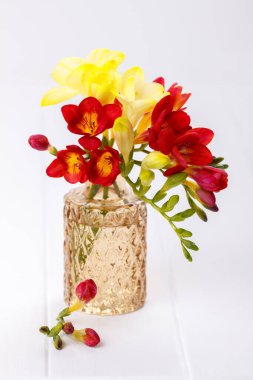 Beyaz ahşap zemin üzerinde sarı ve kırmızı frezyalar buketi, dikey