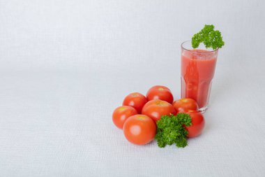 Beyaz arka planda, domates suyu ve domatesli bir bardak maydanozu süslüyor.