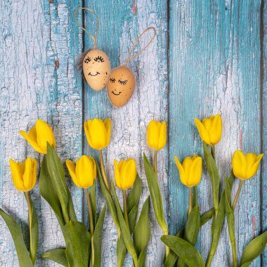 Sarı çiçekler ve yumurtaların bahar kompozisyonu mavi arka planda boyalı şirin bir yüz. Paskalya için tebrikler. Acil