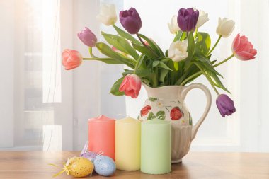 Pencerenin arkasında çiçek açan laleler, mumlar, Paskalya yumurtaları. Paskalya için tebrikler, Mutlu Paskalyalar.