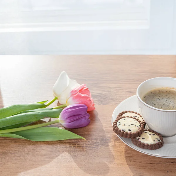 Cup with coffee, cookies and tulips by the window Concept, spring is coming, congratulations on the spring holidays