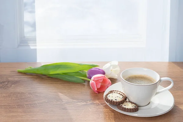 Cup with coffee, cookies and tulips by the window Concept, spring is coming, congratulations on the spring holidays