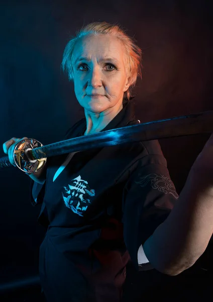 Woman in kimono and Japanese sword, katana Woman, model after 60, in the studio, dark background