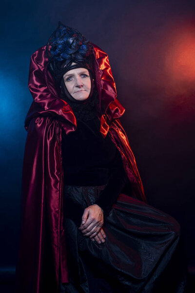 Fabulous creature, historical character, fantasy queen, witch, in costume. Woman, model after 60, in the studio, dark background