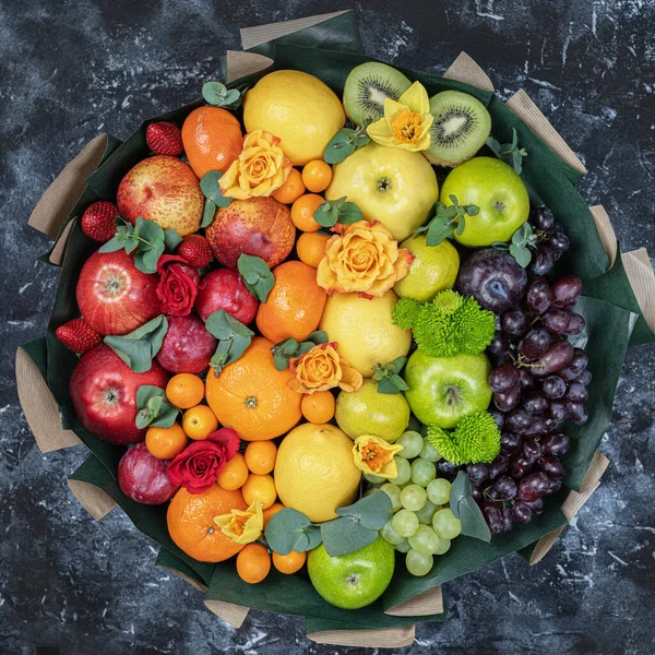 A large bouquet of fruits. Grapes, apples, oranges, kiwi, tangerines, pomegranates and flowers. View from above .