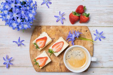 Olgun, kırmızı çilek, süzme peynirli turta, kahve, masada kardelen. Masada hala hayat var.