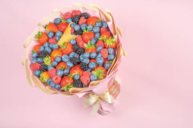 Yenilebilir taze böğürtlen buketi, yabanmersini, ahududu, çilek, pembe arka planda kirpi. Kullanışlı hediye kavramı için bir yer var. Tatil için tebrikler..
