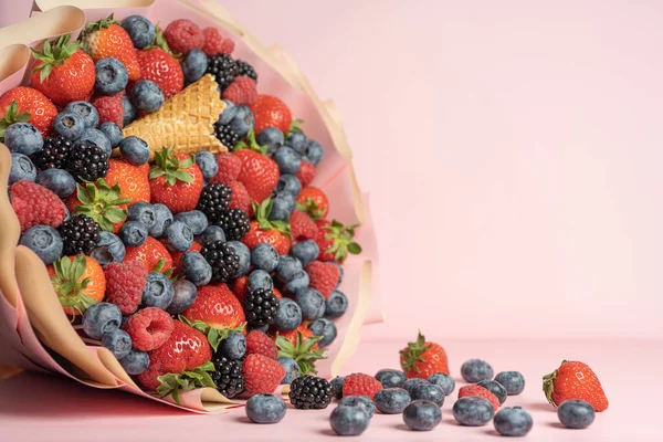 Edible bouquet of fresh berries, blueberries, raspberries, strawberries, hedgehog on a pink background with scattered berries. View from the top .Close-up .Concept of a useful gift, congratulations on the holiday.