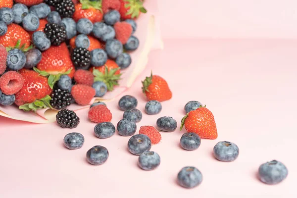 Edible bouquet of fresh berries, blueberries, raspberries, strawberries, hedgehog on a pink background with scattered berries. View from the top .Close-up .Concept of a useful gift, congratulations on the holiday.