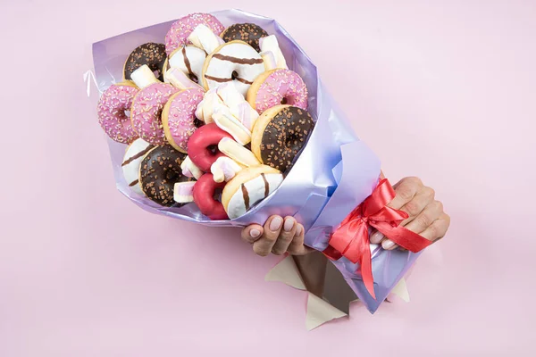 Edible bouquet of donuts and muffins in hand on a pink background. There is a place for text Concept of a sweet gift, congratulations on the holiday.