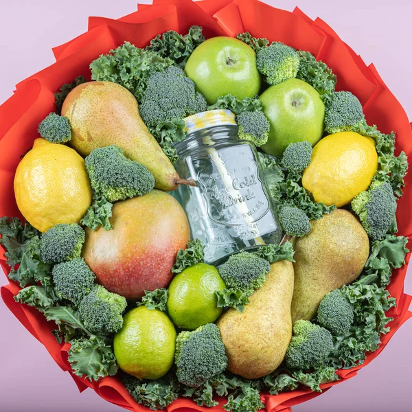 edible fruit and vegetable bouquet with glass smoothie jar, on pink paper background. Concept for advertising, congratulations, recipe.