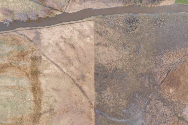 Nehrin kıvrımları, küçük bir nehrin yatağı. Bir İHA 'dan fotoğraf. Finlandiya. Baharın başında İskandinav doğası. Çayırlarda sarı çimenler, çıplak ağaçlar.