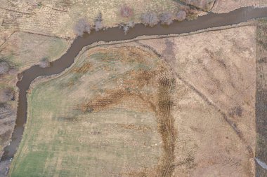 Nehrin kıvrımları, küçük bir nehrin yatağı. Bir İHA 'dan fotoğraf. Finlandiya. Baharın başında İskandinav doğası. Çayırlarda sarı çimenler, çıplak ağaçlar.