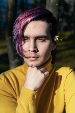 Kulağının arkasında çiçek olan genç bir adam, güneşli bir gün. Parkta. yakın plan