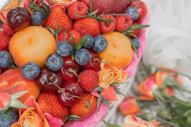 Battaniyenin üzerinde bir sepet dolusu meyve, bir buket gül ve bir bayanın yaz şapkası.