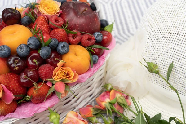 On a blanket a Basket with fruits, a bouquet of roses and a lady\'s summer hat.Natural background.There is a place for text
