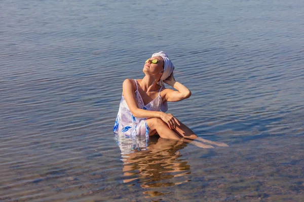 Young woman with cucumbers on her eyes and a towel on her head. Lady sits in the sea .Concept of summer vacation, skin care and health, relaxation, spa