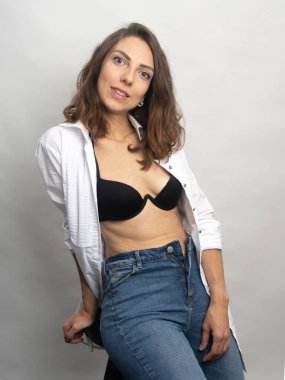 Model, esmer, stüdyoda beyaz arka planda poz veren. Beyaz bir gömlek giyiyor, siyah bir saç stili. Bele fotoğraf.