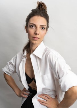 Model, esmer, stüdyoda beyaz arka planda poz veren. Beyaz bir gömlek giyiyor, siyah bir saç stili. Bele fotoğraf.