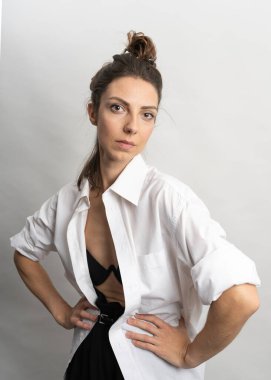 Model, esmer, stüdyoda beyaz arka planda poz veren. Beyaz bir gömlek giyiyor, siyah bir saç stili. Bele fotoğraf.