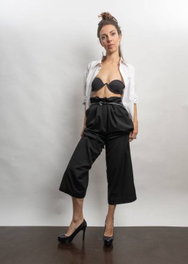 Model, esmer, stüdyoda beyaz arka planda poz veren. Beyaz bir gömlek giyiyor, siyah bir saç stili. Bele fotoğraf.