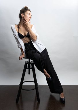 Model, esmer, hasır şapkalı, stüdyoda beyaz arka planda poz veren. Beyaz bir gömlek giyiyor, siyah bir saç stili..