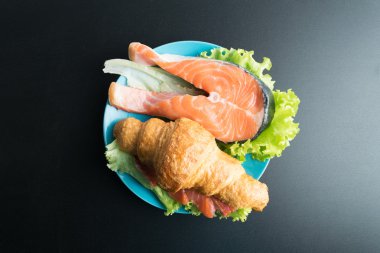 Kruvasan somon ve marul üzerinde siyah backgr mavi plaka üzerinde