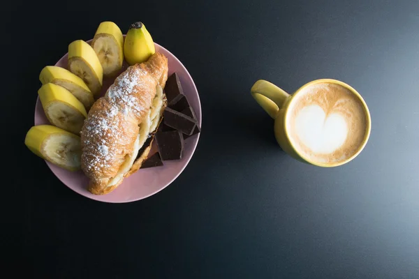 Круасан з шоколадом, бананом на рожевій тарілці та жовтою чашкою — стокове фото