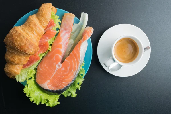Круасан з лососем, салатом на синій тарілці та чашкою кави о — стокове фото