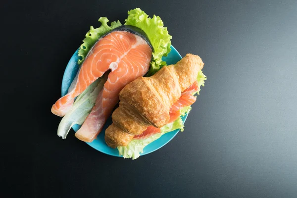 Круасан з лососем і салатом на синій тарілці на чорному фоні — стокове фото