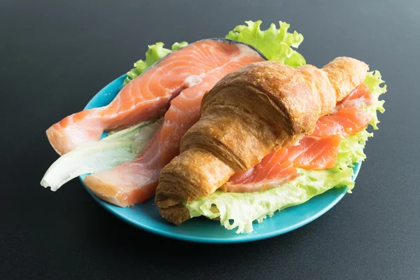 Croissant con salmón y lechuga en plato azul sobre fondo negro —  Fotos de Stock