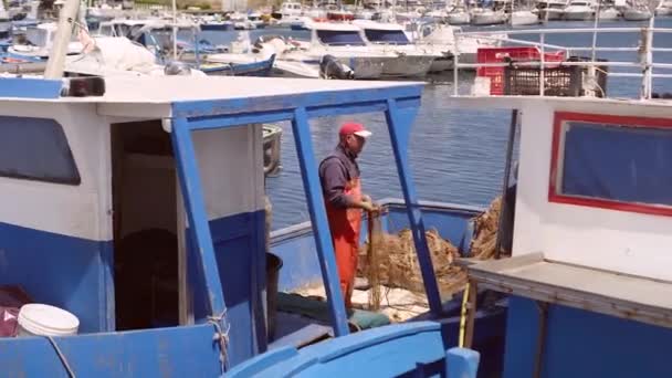 Debonair rybář rozmotává síť, stojí na rybářské lodi v přístavu — Stock video