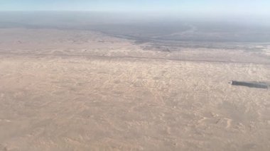 Yukarıdan görülen uçsuz bucaksız bir çöl manzarası. Kum desenli ve atmosferik sisli doğal kurak arazi. Seyahat, doğa ve çevre kavramı.