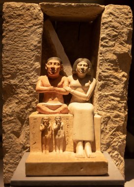 Kahire, Mısır; 21 Ocak 2024: Kahire 'deki Mısır Müzesi' nde Antik Mısırlı cenaze çifti heykeli sergilendi. Kireçtaşı heykel, eski Mısır mezarının ortak bir unsuru olan sembolik sahte bir kapının içine yerleştirilmiş bir erkek ve kadını gösteriyor.