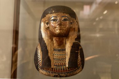 Kahire, Mısır; 21 Ocak 2024: Kahire, Mısır 'da bir müze cam kutusunda sergilenen Antik Mısırlı boyalı cenaze maskesi. Görüntü, detaylı işçiliği, korunmuş pigmentleri ve eğitim ve editörlüğe uygun tarihi gömme sanatını gösteriyor..